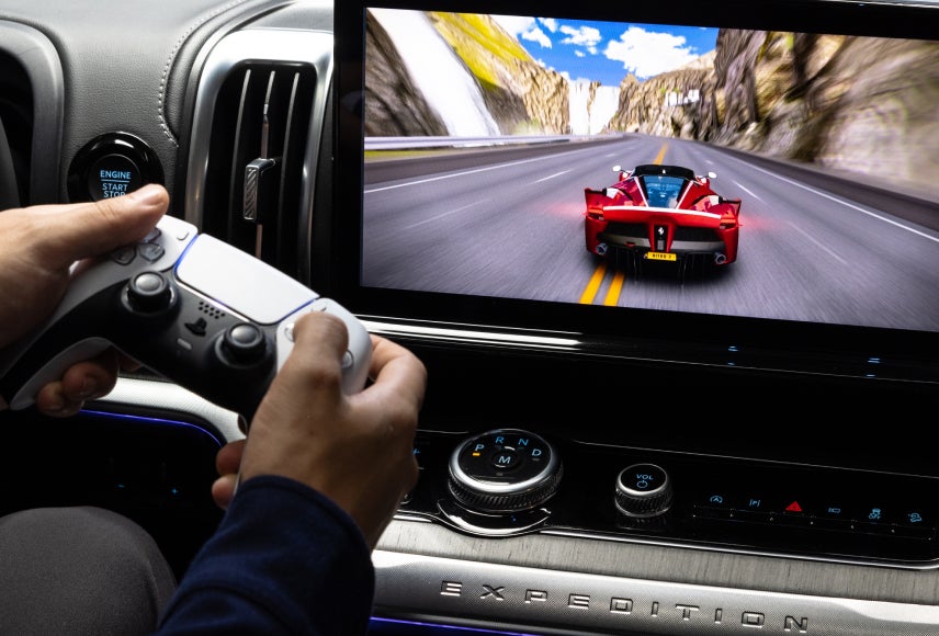 A Ford vehicle technology screen displays Asphalt Nitro 2 while a passenger uses a controller to play. Screen may vary.