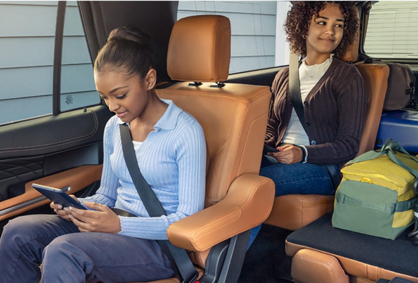Two smiling children using mobile devices while sitting in the second and third rows of a Ford SUV.